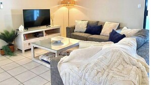 A living room with a sofa, TV, and a lamp. - 5 mins walk to town and beach. Family sized top floor condo! (Port Douglas)