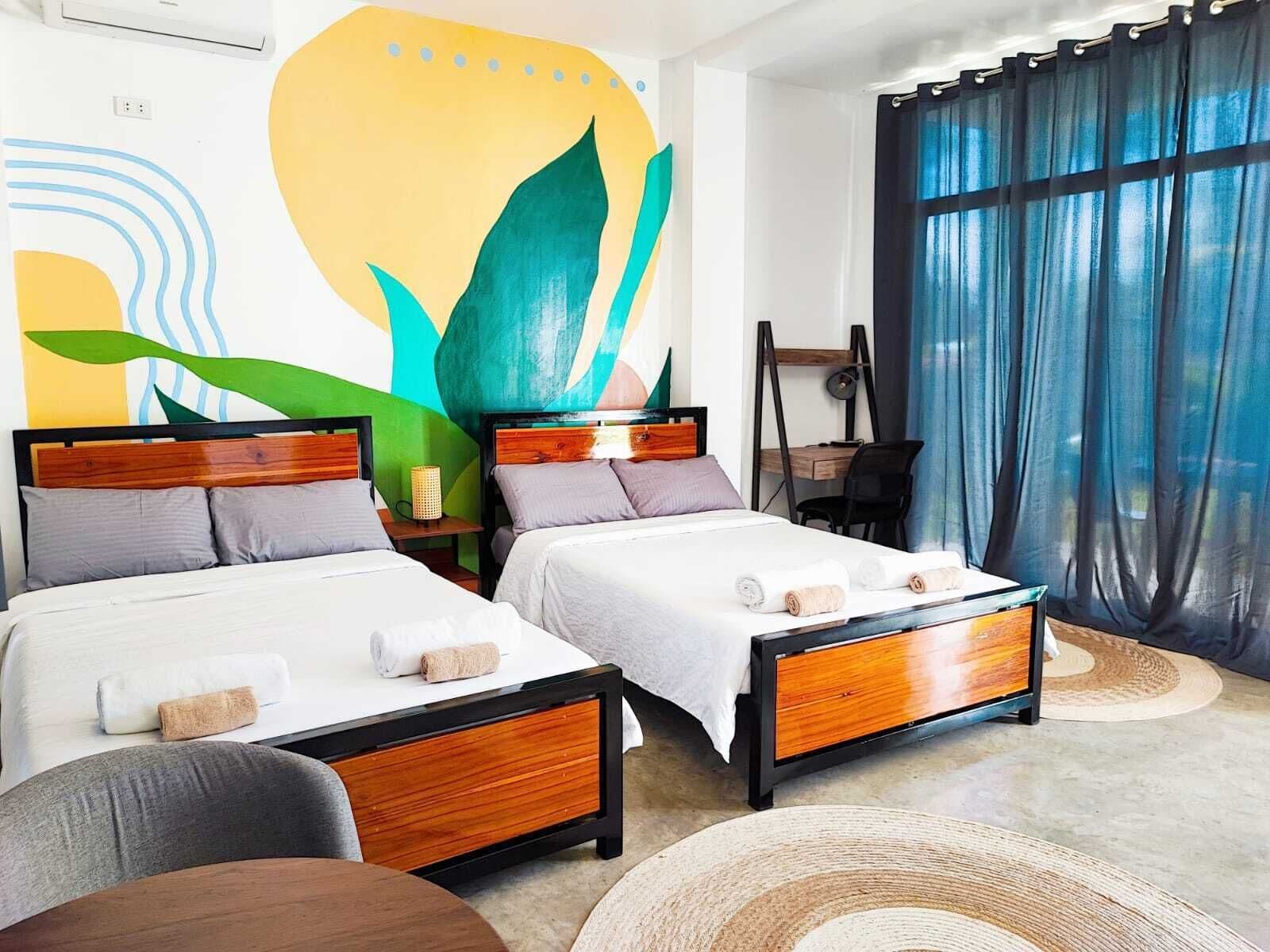Habitación de hotel con dos camas, un escritorio y un ventanal grande con cortinas.