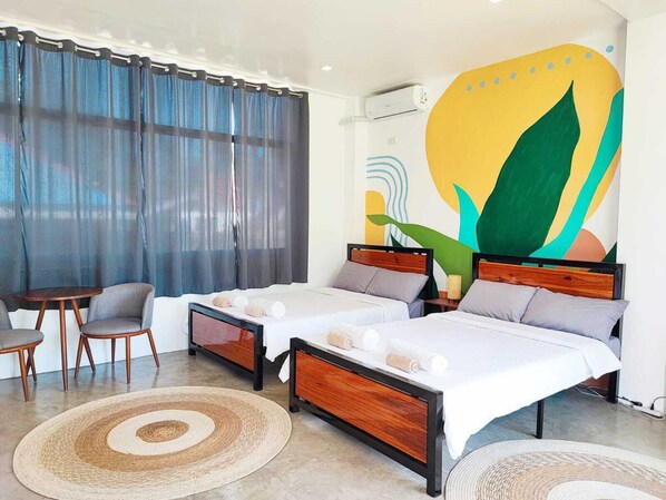 A hotel room with two beds, a small table, chairs, and a large abstract painting on the wall.