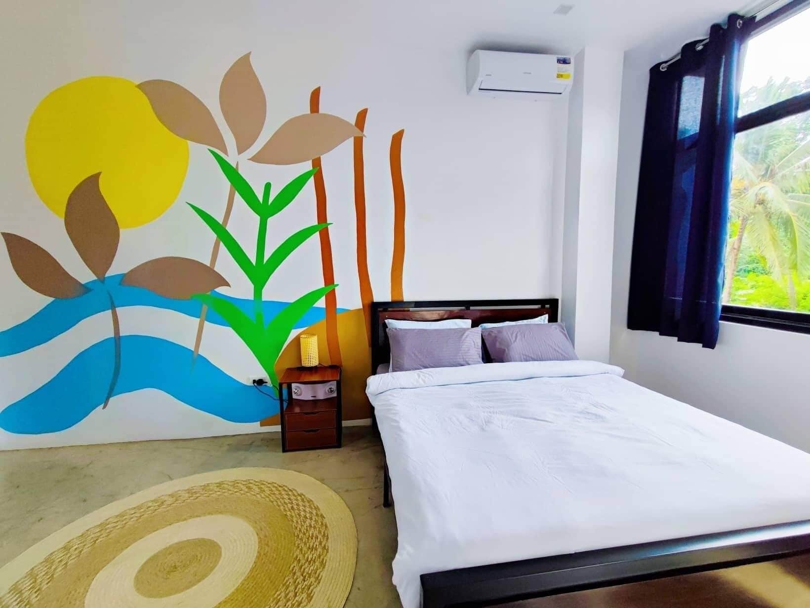 A bedroom with a bed, a nightstand, a wall mural, an air conditioner, and a window with curtains.