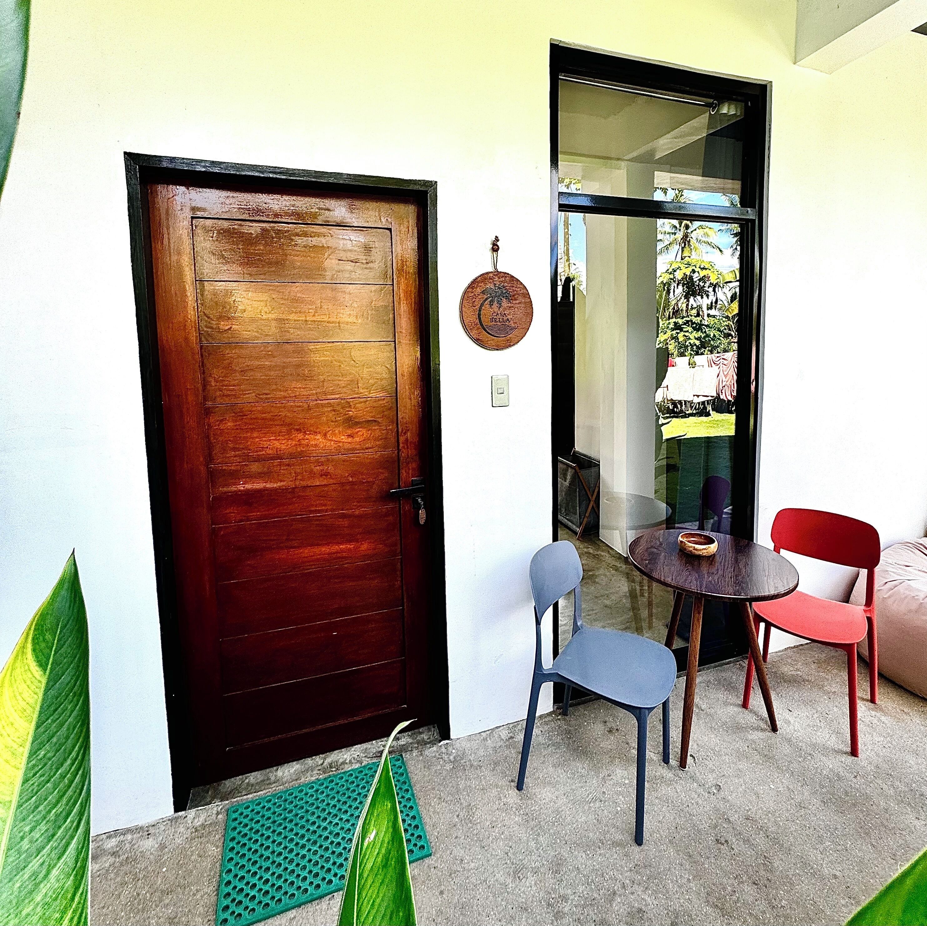 Uma porta de madeira, uma porta de vidro, uma pequena mesa com cadeiras e um tapete verde.