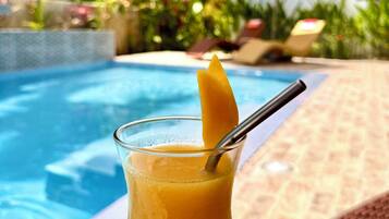 Un vaso de jugo de naranja con una rodaja de naranja y una pajita, sobre una silla de mimbre junto a una piscina.