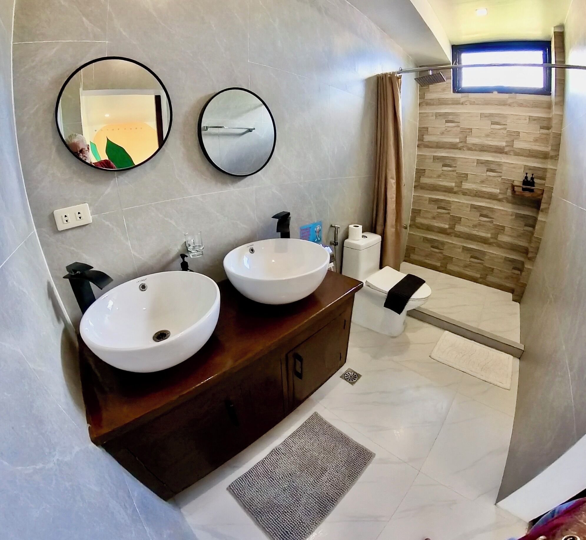 Un baño moderno con dos lavamanos, un tocador, ducha y ventana.