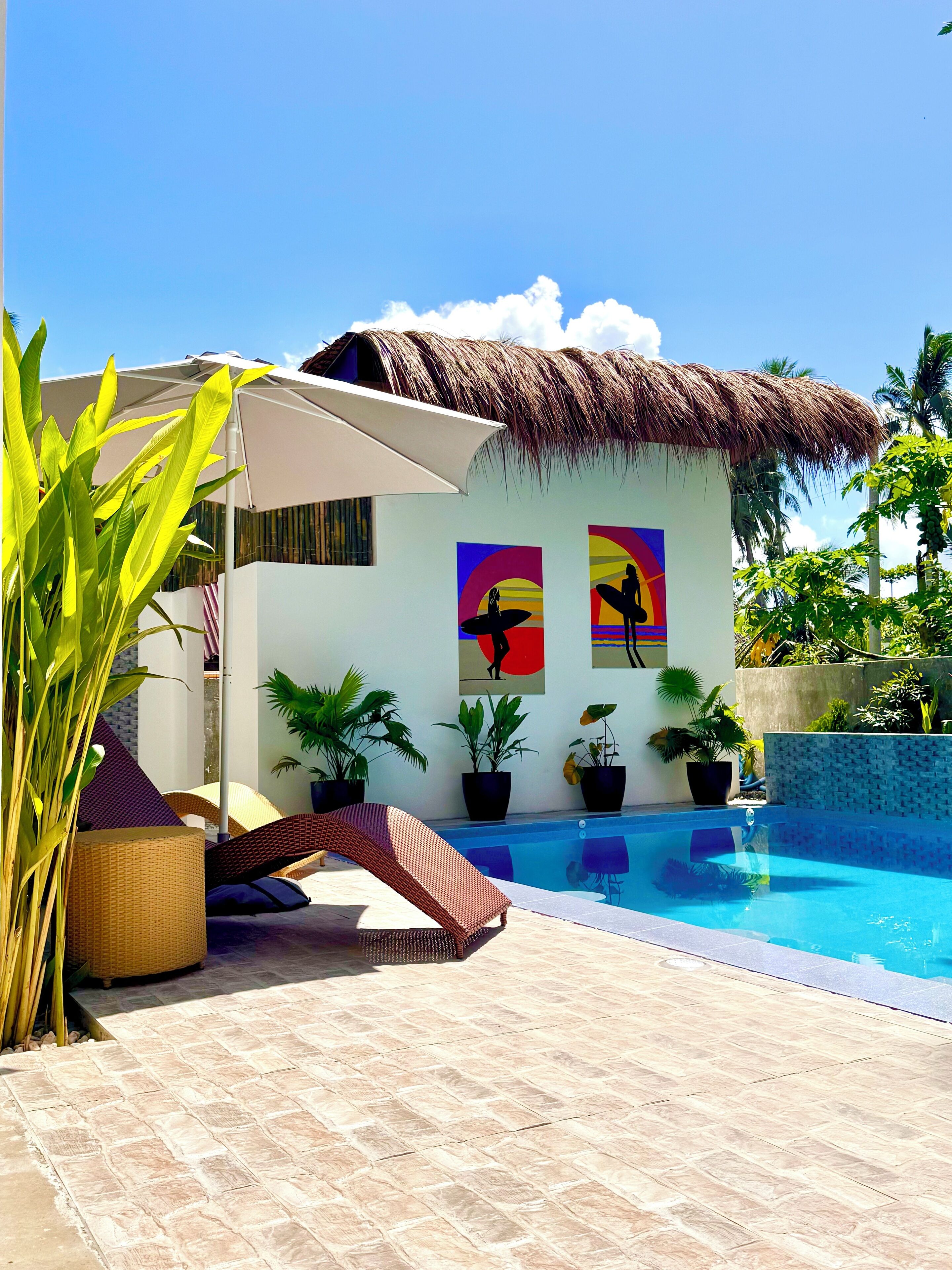 A pool area with a thatched-roof structure, lounge chairs, and potted plants.