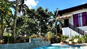 A swimming pool with clear blue water, surrounded by lush greenery and palm trees. - Casa Basa Siargao (General Luna)