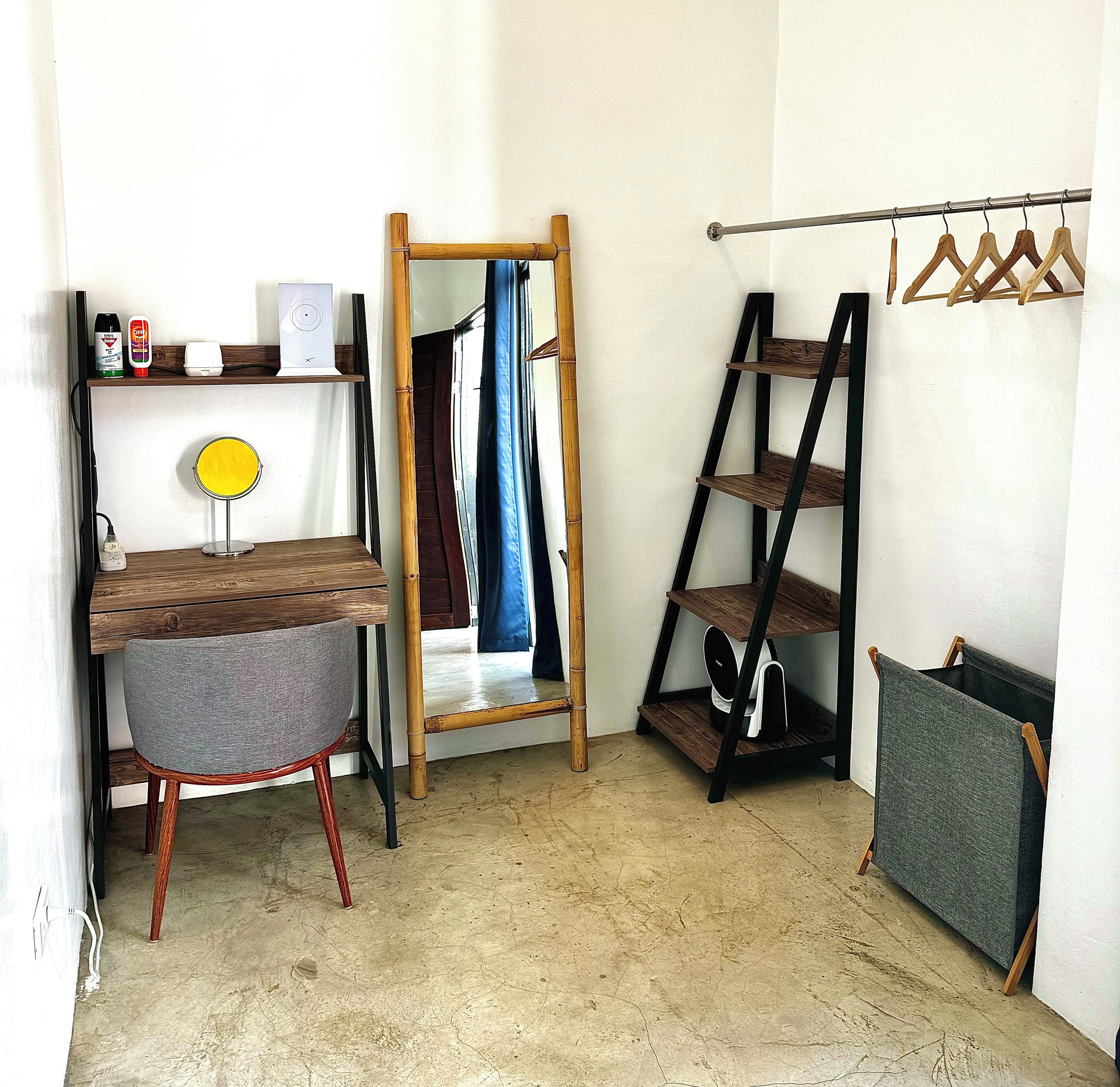 Una habitación con un escritorio de madera, una silla, un espejo, un estante con productos de limpieza, un perchero y un separador plegable.