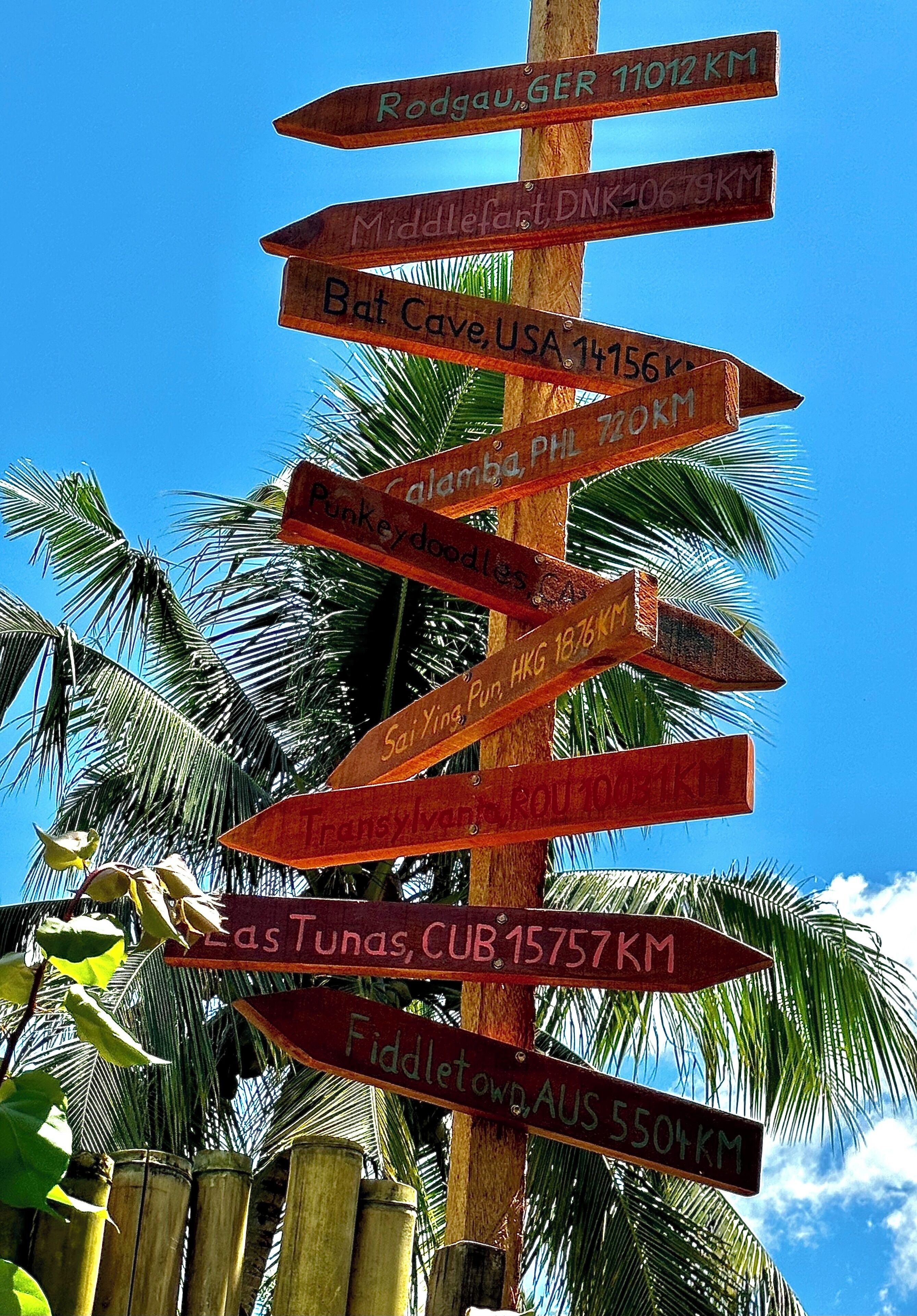 A wooden signpost with multiple directional signs pointing to various global destinations and distances in kilometers.