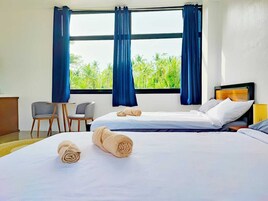 Habitación de hotel con dos camas, un escritorio, sillas y vista a palmeras.