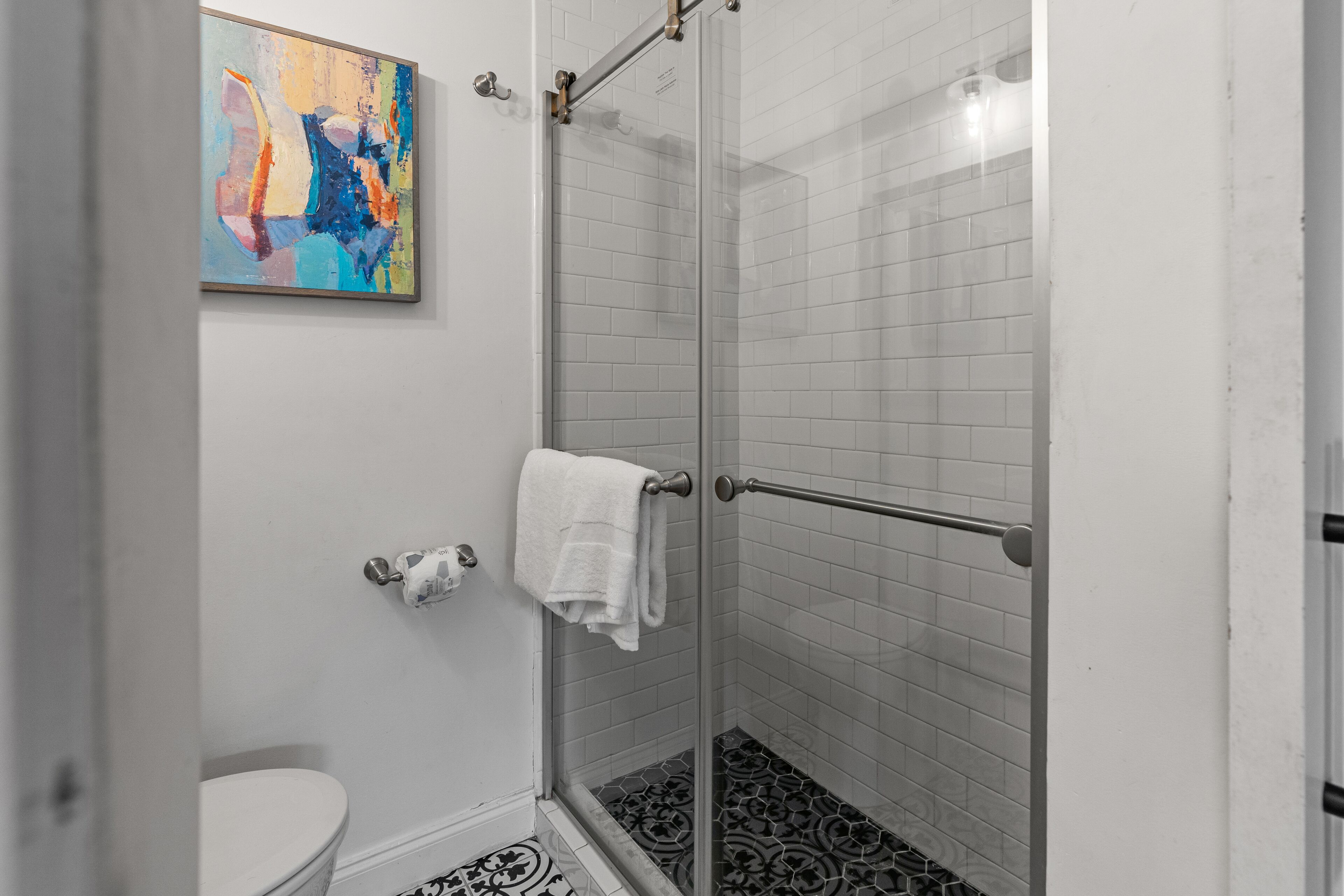 A bathroom with a glass shower enclosure, a toilet, and a towel rack.