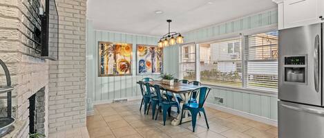 A kitchen with a brick wall, a dining table with chairs, a refrigerator, and a window with blinds.
