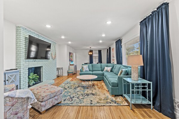 Un salon avec un canapé de couleur turquoise, une table basse ronde, un tapis à motifs, une cheminée et un téléviseur fixé à un mur en briques.