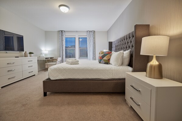 A bedroom with a bed, bedside table, lamp, and a dresser.