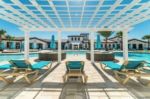 A poolside area with lounge chairs and umbrellas, a covered seating area, and a building in the background.