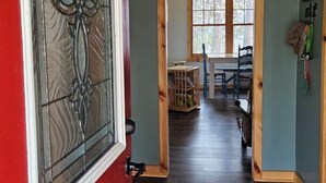 Un vano de puerta de madera que da a un comedor con una mesa, sillas y un banco de madera, y un letrero que dice 'Welcome to the Lake' sobre la puerta.