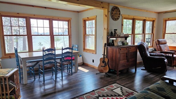 Una habitación acogedora con una mesa de comedor de madera, sillas azules, una guitarra, un sillón de cuero y un ventanal con vistas a árboles.