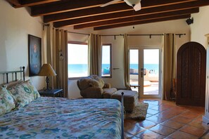 Een slaapkamer met een bed, een stoel, een lamp en uitzicht op het strand.