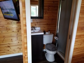 Puisesta mökistä löytyvä kylpyhuone, jossa on pesuallas, wc ja suihku.