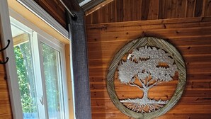 Ein kleines Schlafzimmer mit Fenster, einem Bett, einem kleinen Tisch und einer Wanddekoration mit Baumotiv.