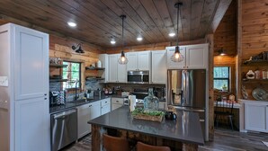 A modern kitchen with stainless steel appliances, wooden cabinets, and a central island. - 3 BR Luxury Cabin & Hot Tub near Buffalo River! (Jasper)