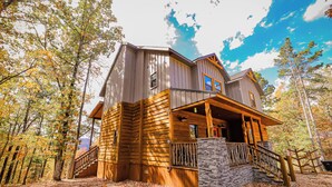A log cabin with a stone staircase and wooden railing, surrounded by autumn trees. - 3 BR Luxury Cabin & Hot Tub near Buffalo River! (Jasper)