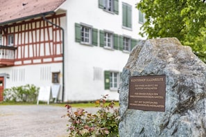 En stentavla med text, en traditionell byggnad med korsvirkesfasad och ett träd i förgrunden.