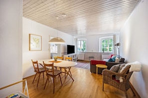 Ett modernt vardagsrum med en matplats, trägolv, en tv och en fåtölj i rotting.