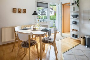 A dining area with a table set for four, chairs with fur throws, a radiator, and a view of a house through a window. - Holiday Apartment "Weitblick" with Mountain View, Balcony & Wi-Fi (Breitnau)