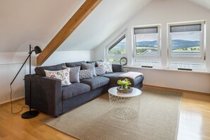 A modern living room with a sectional sofa, a floor lamp, a round coffee table, and a view of the countryside through large windows. - Holiday Apartment "Weitblick" with Mountain View, Balcony & Wi-Fi (Breitnau)