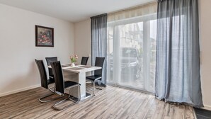 A modern room with a dining table, four chairs, a vase with flowers, a painting on the wall, and a large window with curtains. - Apartment 'Familie Richter' with Wi-Fi (Lahr)