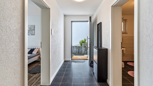 A hallway with a bed, a door leading to a balcony, and a bathroom with a toilet and sink. - Apartment 'Familie Richter' with Wi-Fi (Lahr)