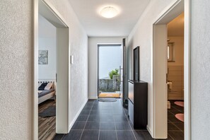 Un couloir avec un lit, une porte donnant sur un balcon et une salle de bain équipée de toilettes et d’un lavabo.