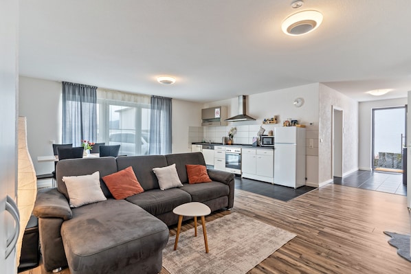 A modern living room with a grey sofa, a small table, and a kitchen in the background.