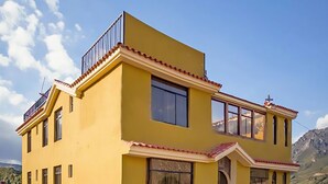 A multi-story yellow building with balconies and a stone-paved ground. - Colibri Inn (Chivay)