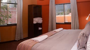 Habitación de hotel con cama, un armario y dos ventanas con cortinas.