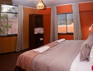 A hotel room with a bed, a wardrobe, and two windows with curtains.