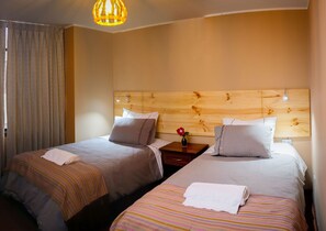 A hotel room with two beds, each with a wooden headboard, a nightstand, a vase with a flower, and a striped blanket.