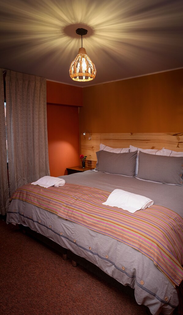 A neatly made bed with a striped bedspread, a wooden headboard, and a hanging light fixture. - Colibri Inn (Chivay)