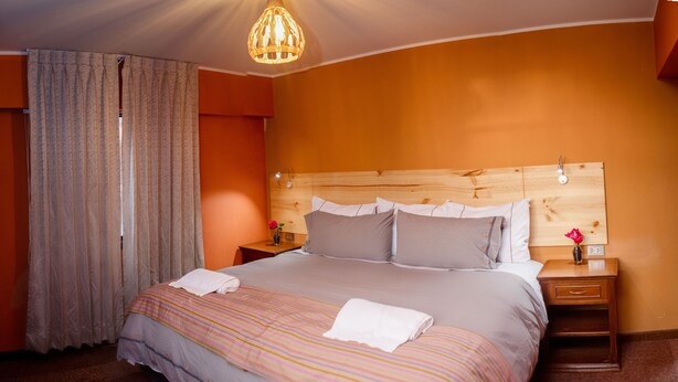A hotel room with a large bed, wooden headboard, and a nightstand with a vase of flowers. - Colibri Inn (Chivay)