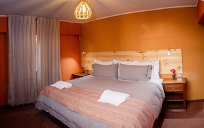 A hotel room with a large bed, wooden headboard, and a nightstand with a vase of flowers. - Colibri Inn (Chivay)
