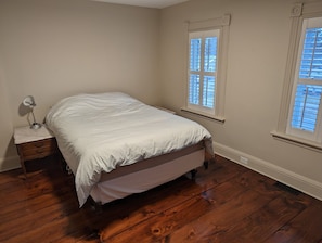 Une chambre à coucher avec un lit, un plancher en bois et deux fenêtres équipées de stores.