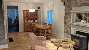 Un ampio soggiorno con un tavolo da pranzo in legno, due poltrone rosa, un camino in pietra e una scala che conduce a un'altra stanza.