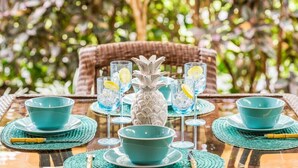 A table set with blue bowls, glasses, and a pineapple centerpiece, surrounded by wicker chairs and greenery.