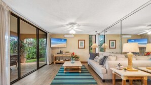 A spacious living room with a large sliding glass door leading to a patio, a ceiling fan, a sofa, a coffee table, and two lamps.