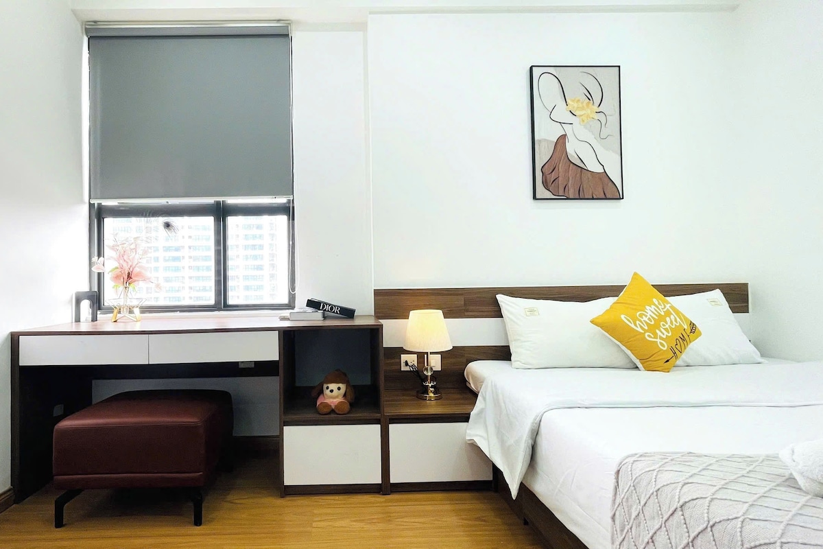 A hotel room with a desk, a bed, a nightstand, and a window with a view of buildings.