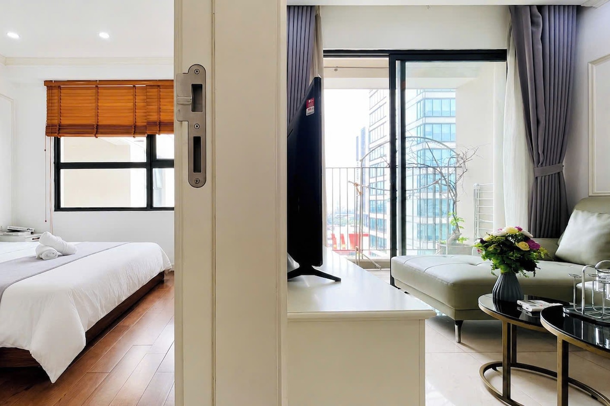 A hotel room with a bed, a sofa, a coffee table, and a window with a view of buildings.