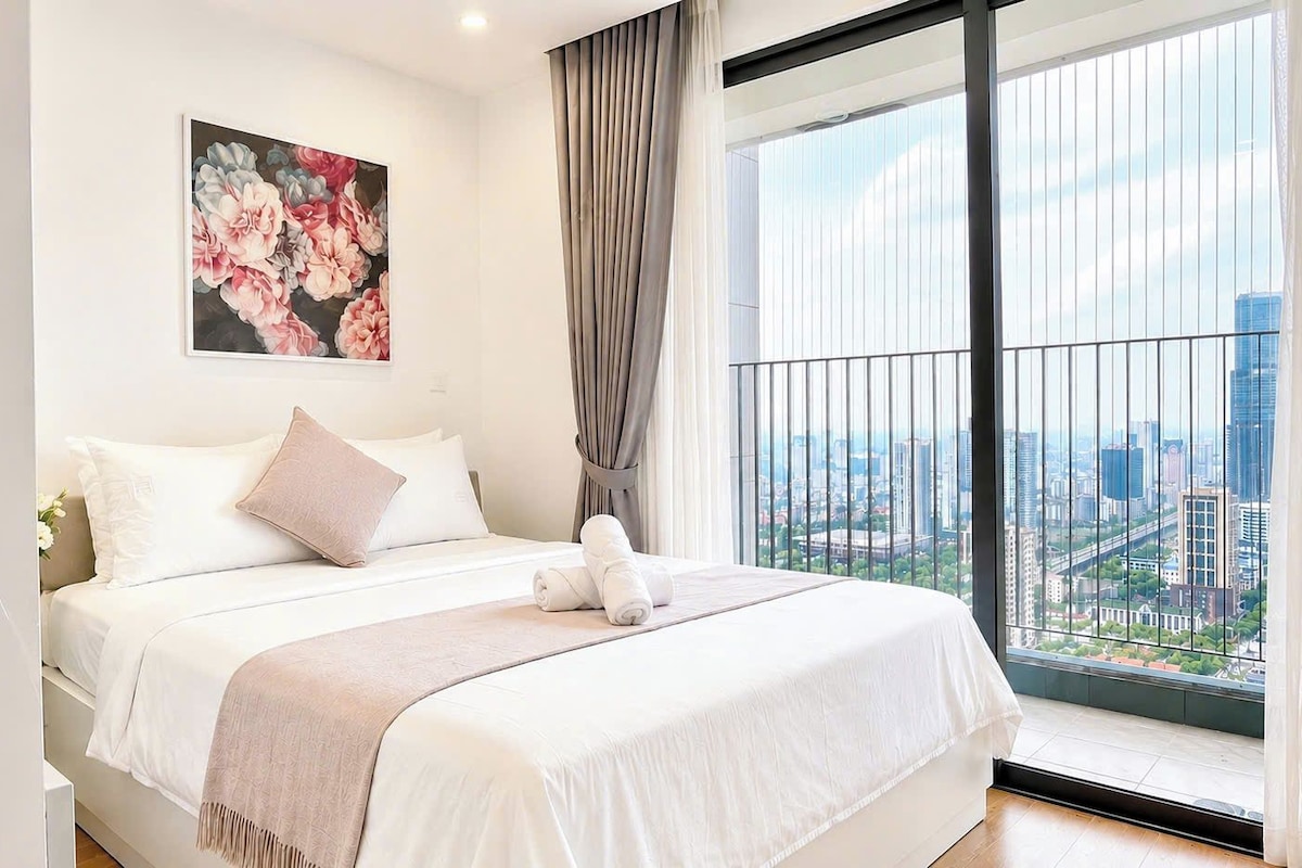 A hotel room with a large bed, a city view, and a painting on the wall.