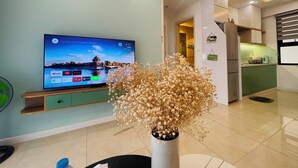 Un soggiorno moderno con una TV a schermo piatto, un vaso decorativo con fiori secchi e una cucina verde sullo sfondo.