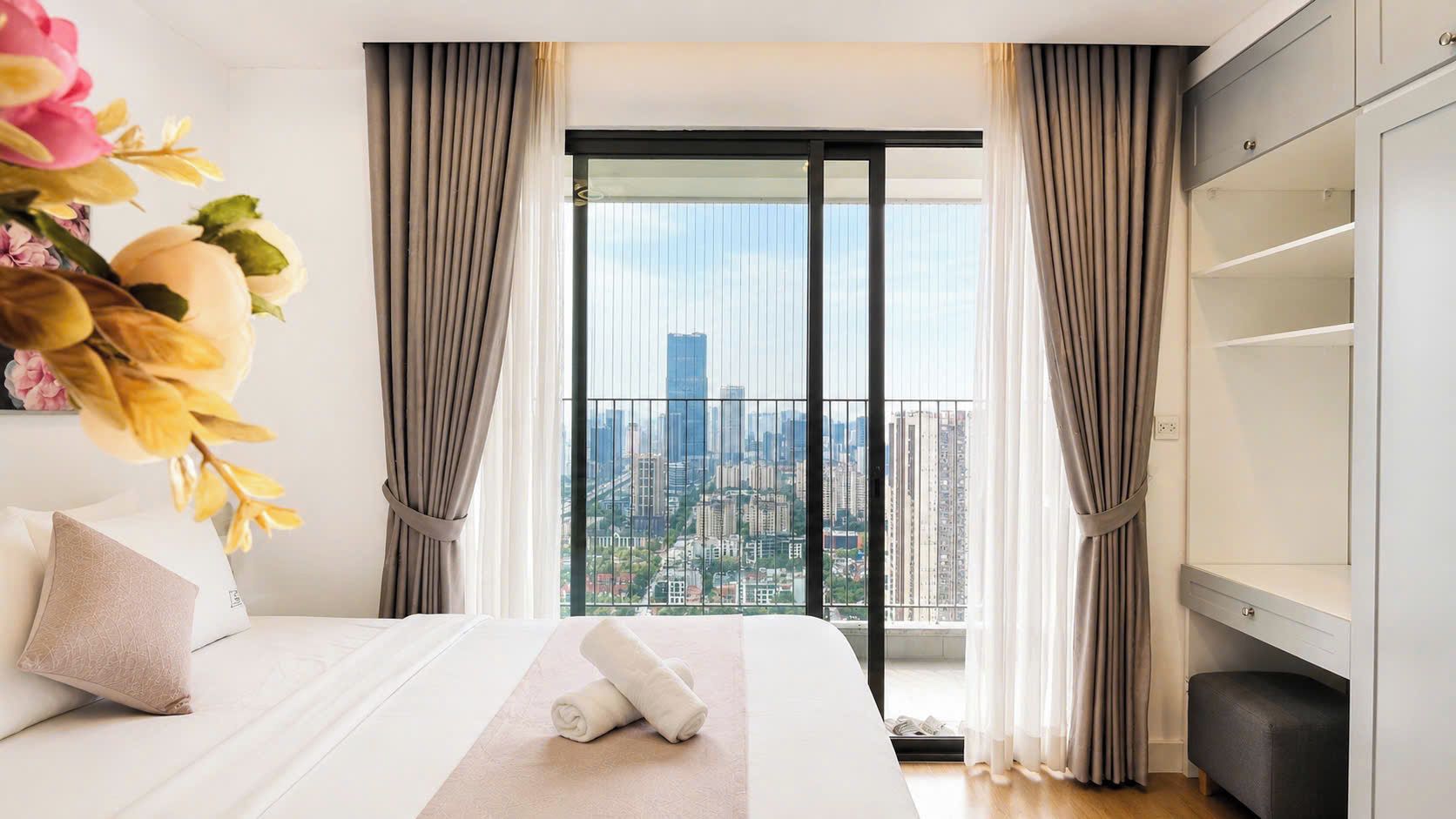 Habitación de hotel con cama, vista de la ciudad a través de un ventanal grande y un armario.