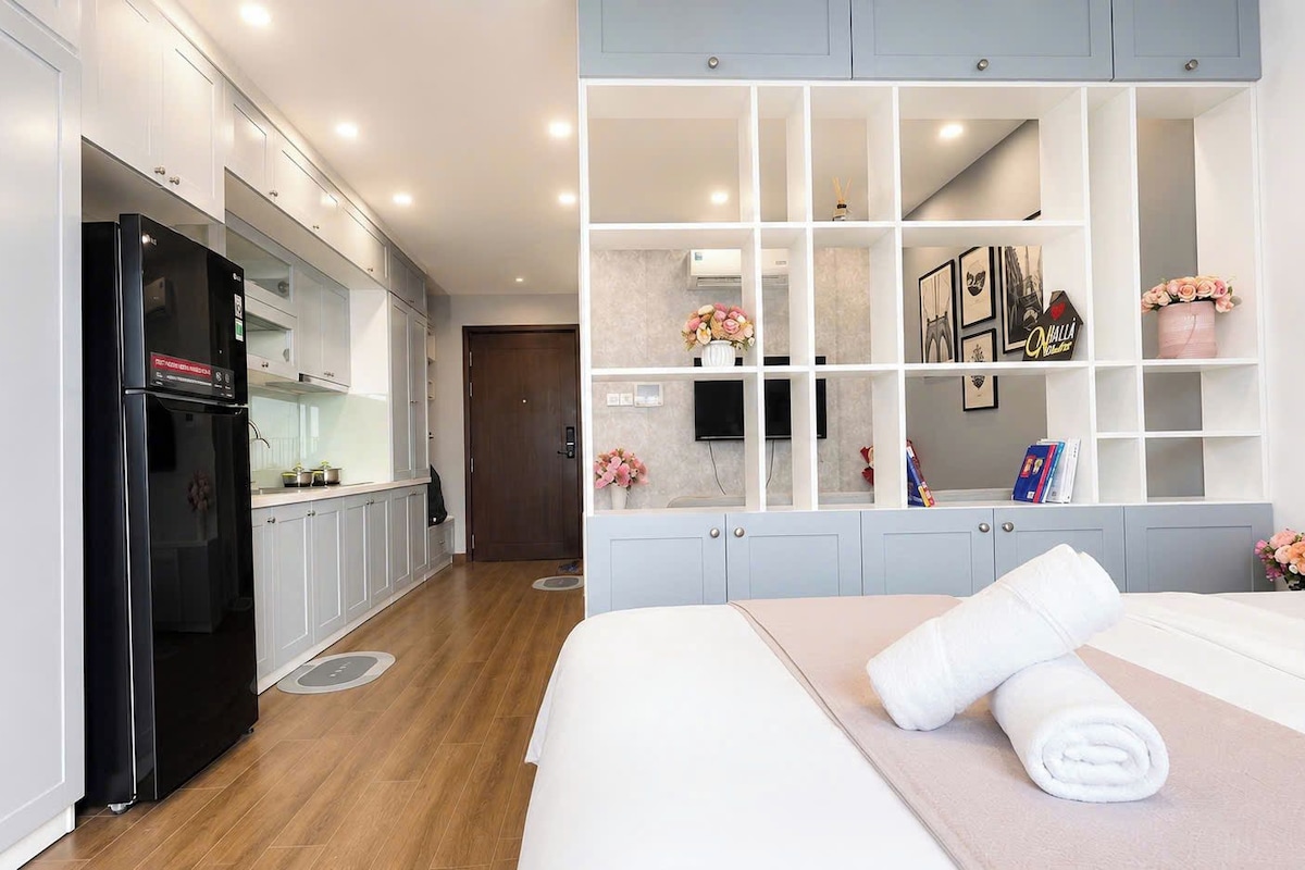 A modern hotel room with a bed, a built-in wardrobe, a kitchenette, and a large window.