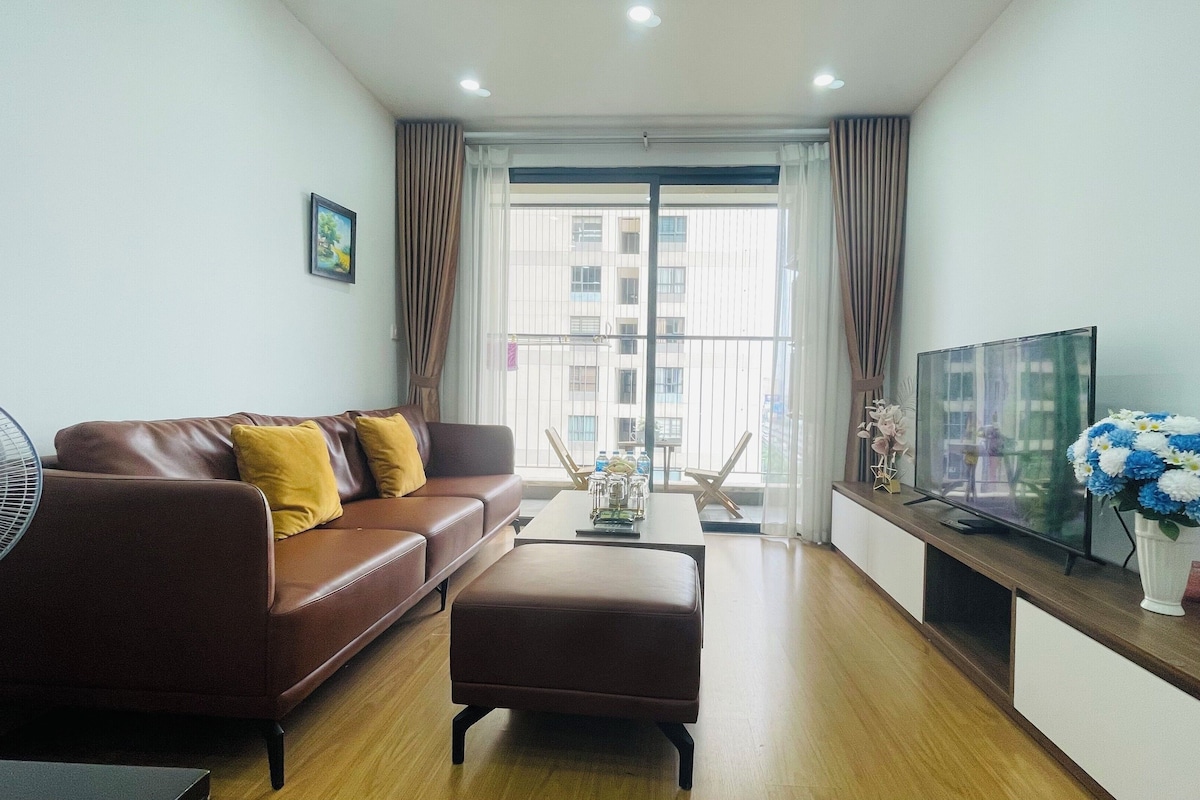 A living room with a brown leather sofa, a coffee table, a TV on a wooden stand, and a fan.